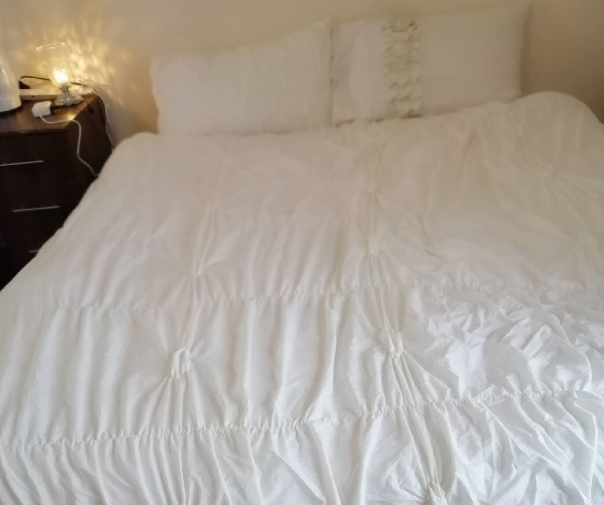 Un lit avec une literie blanche et une lampe sur une table de chevet.