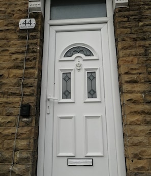 Uma porta branca com placa indicando '44 Balfour Street', uma pequena janela com decoração no topo e uma abertura para correspondência abaixo.