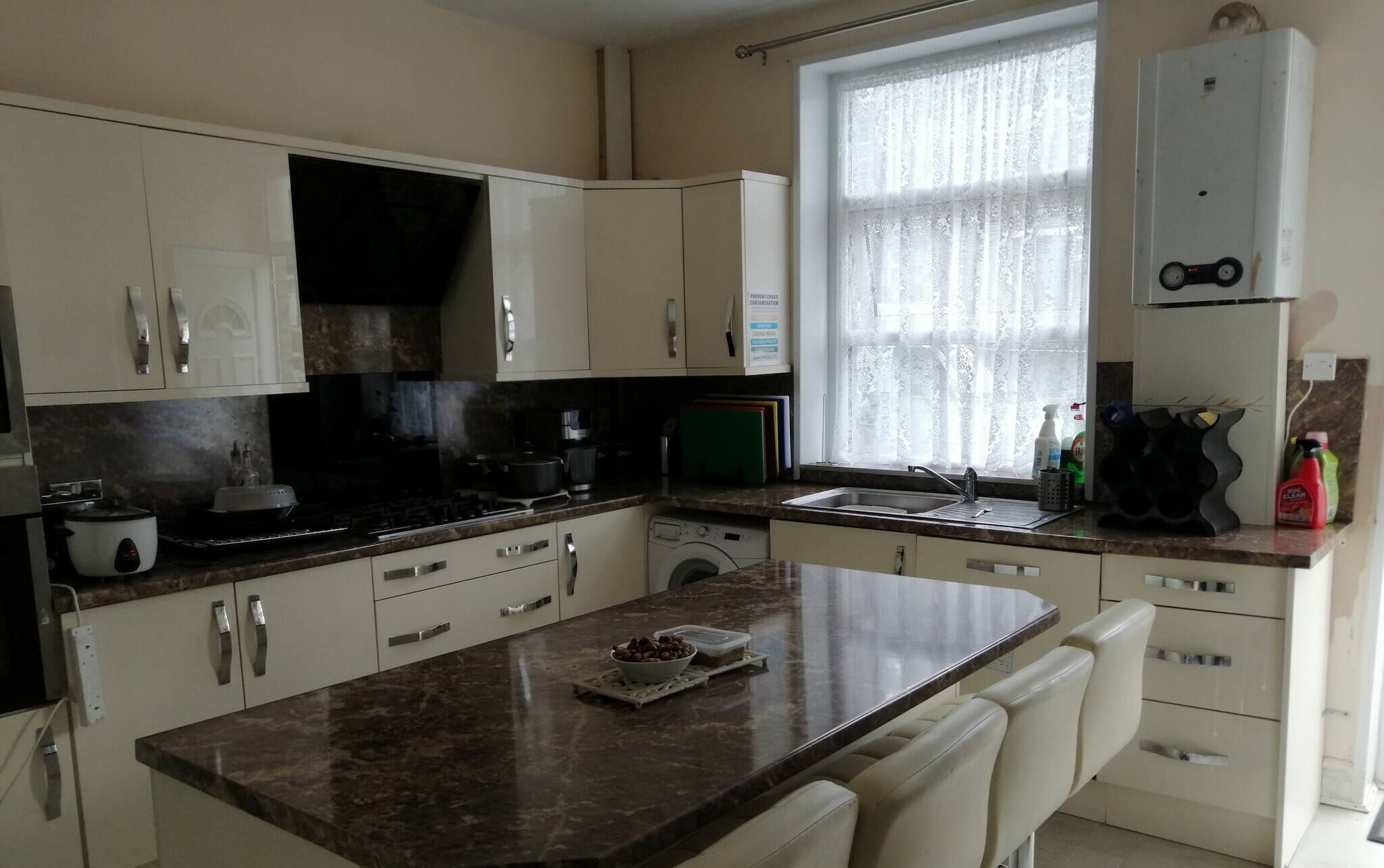 Cozinha com armários brancos, bancada de granito, máquina de lavar embutida e janela com cortinas de renda.