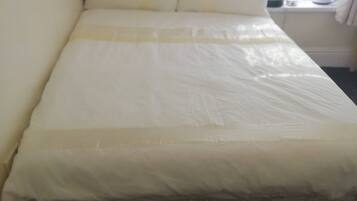 A bed with a white mattress and pillows, a bedside table with a lamp, and a window with curtains.