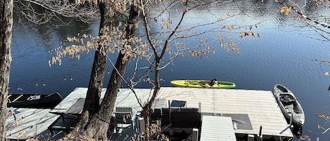 Un muelle con kayaks y una canoa, rodeado de árboles y un lago tranquilo.