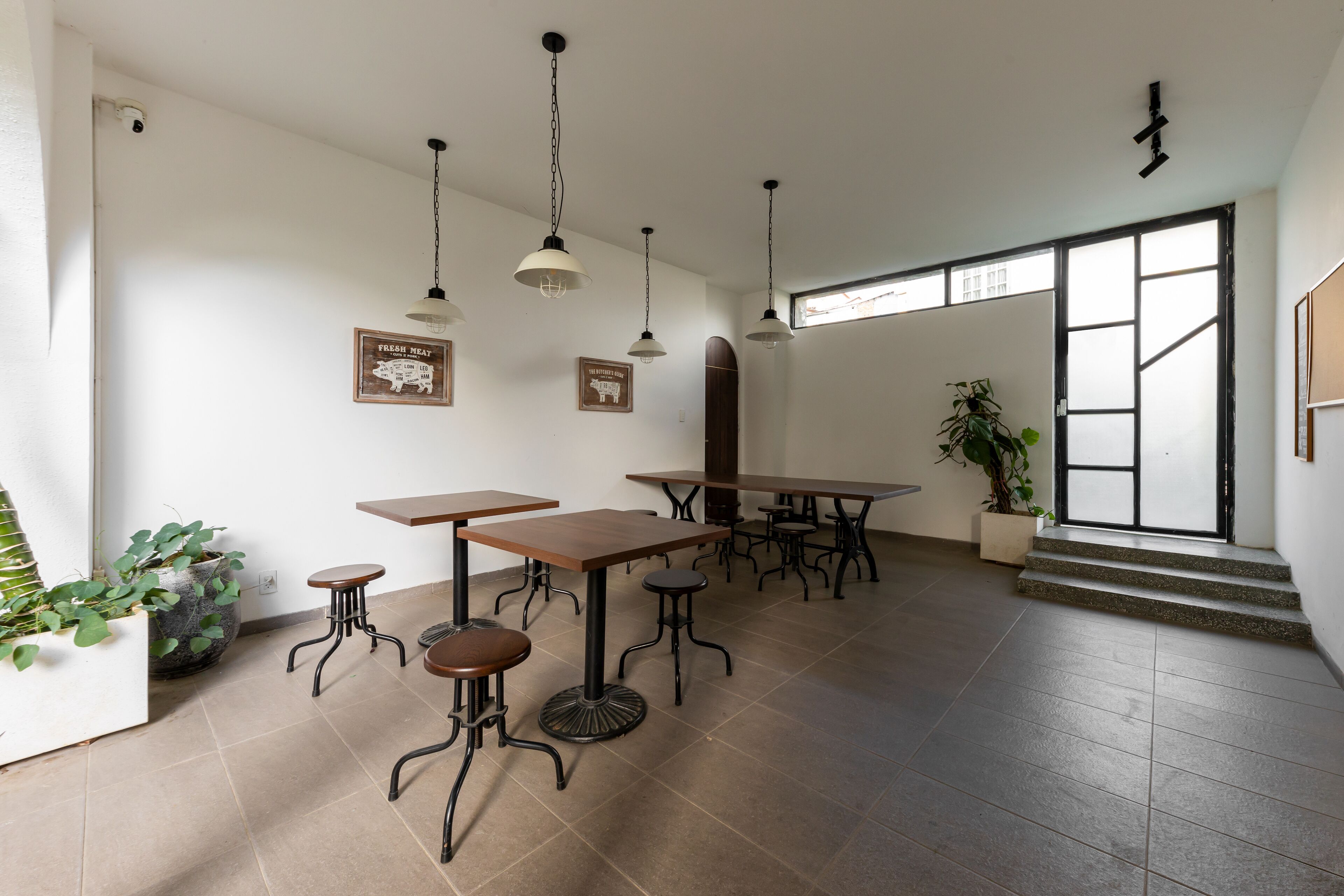 A spacious room with multiple tables and chairs, a large window with a view, and a staircase leading to an upper level.