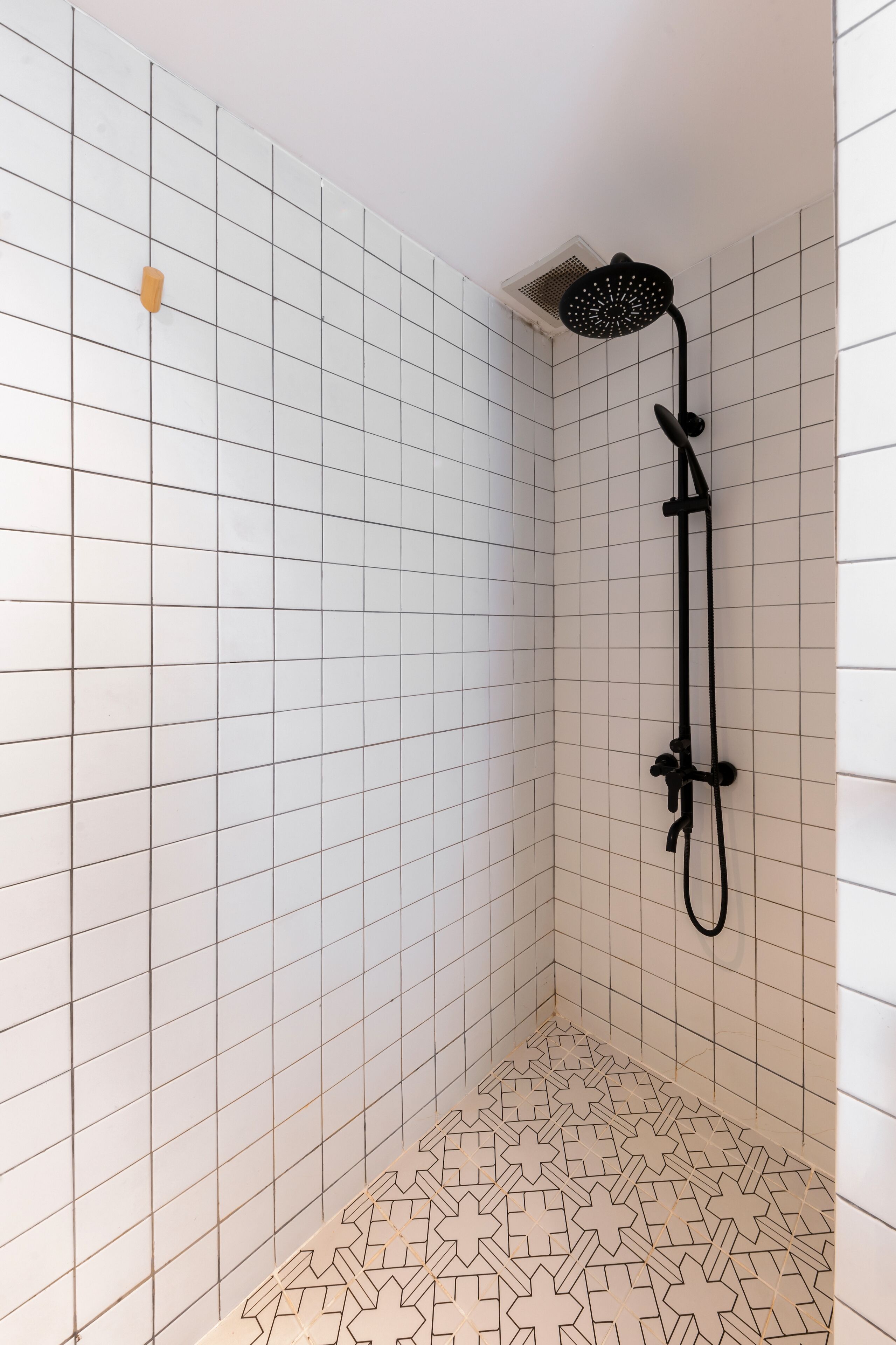 A shower area with white tiled walls and floor, a black showerhead, and a patterned floor design.