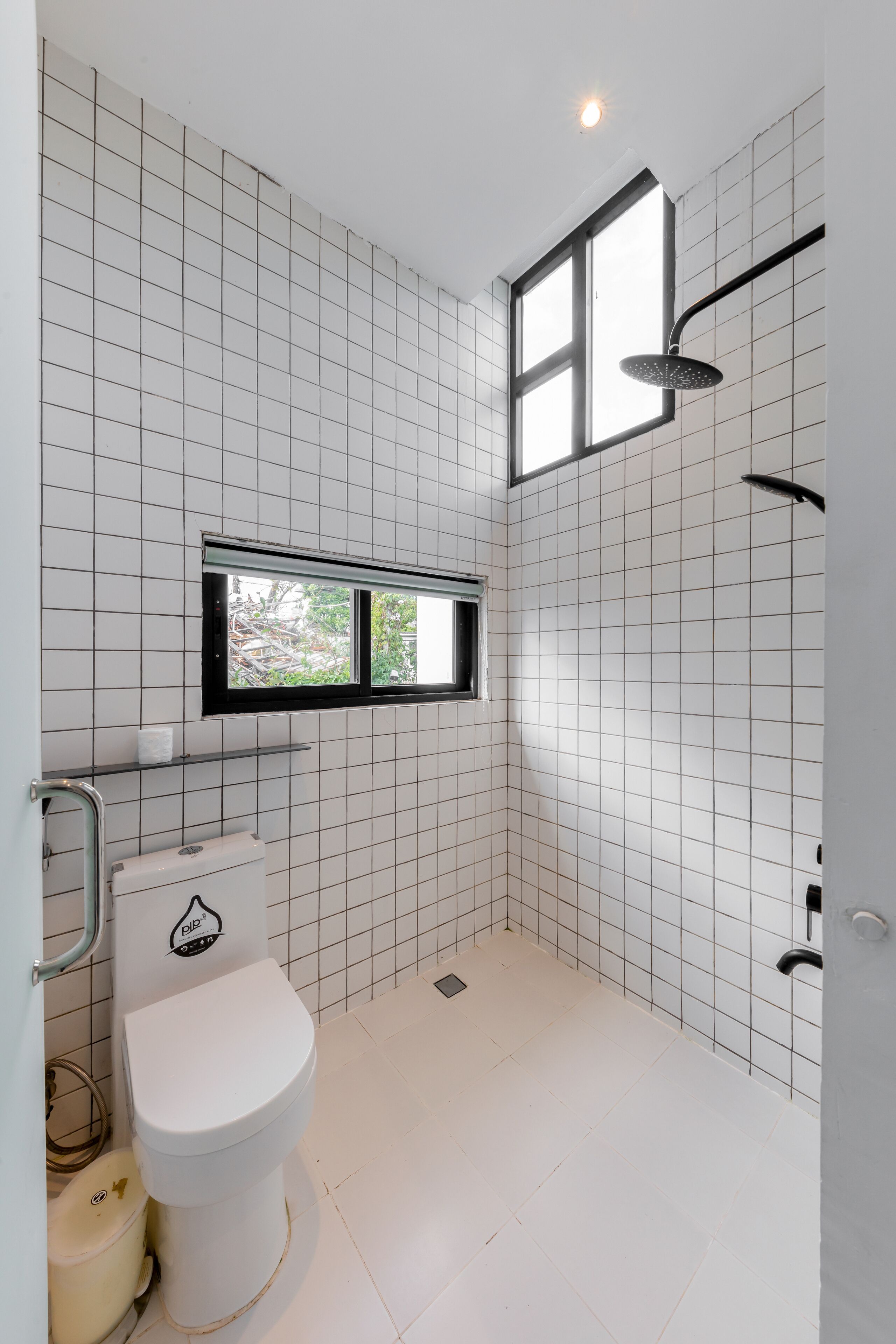 A bathroom with white tiled walls, a toilet, a window, and a shower.