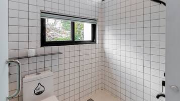 A bathroom with white tiled walls, a toilet, a window, and a shower.