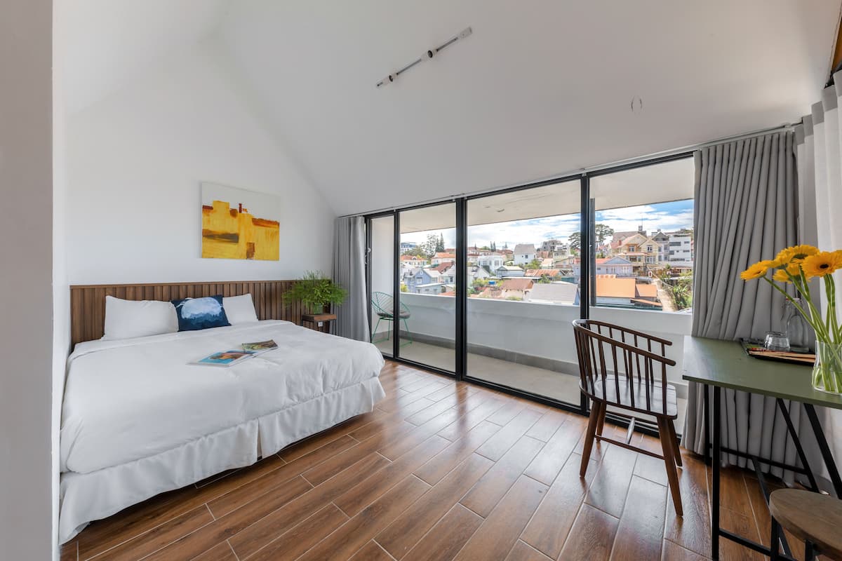 A modern hotel room with a large bed, a dining area, and a balcony with a city view.