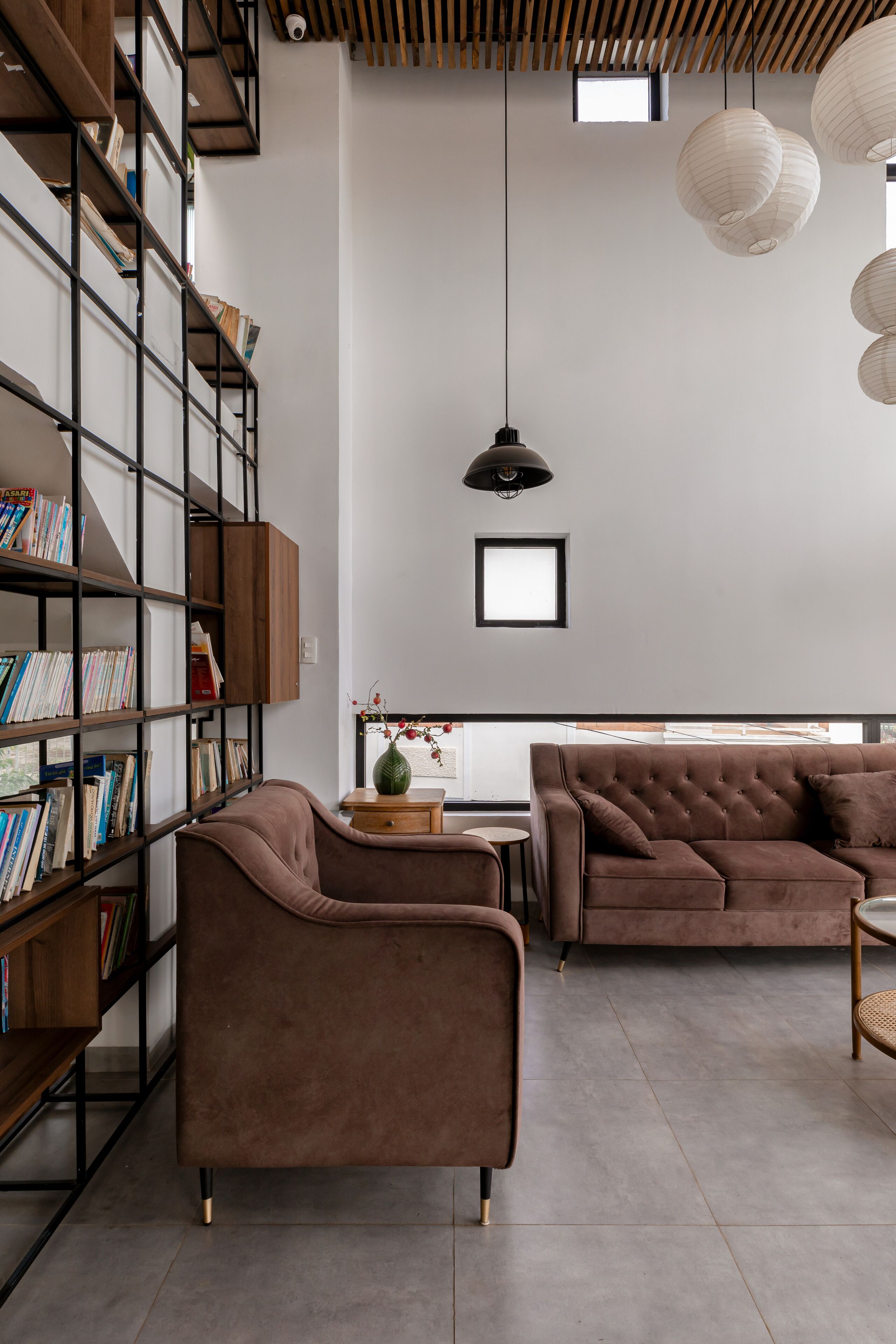 A modern living room with a brown sofa, a bookshelf, and a dining area.