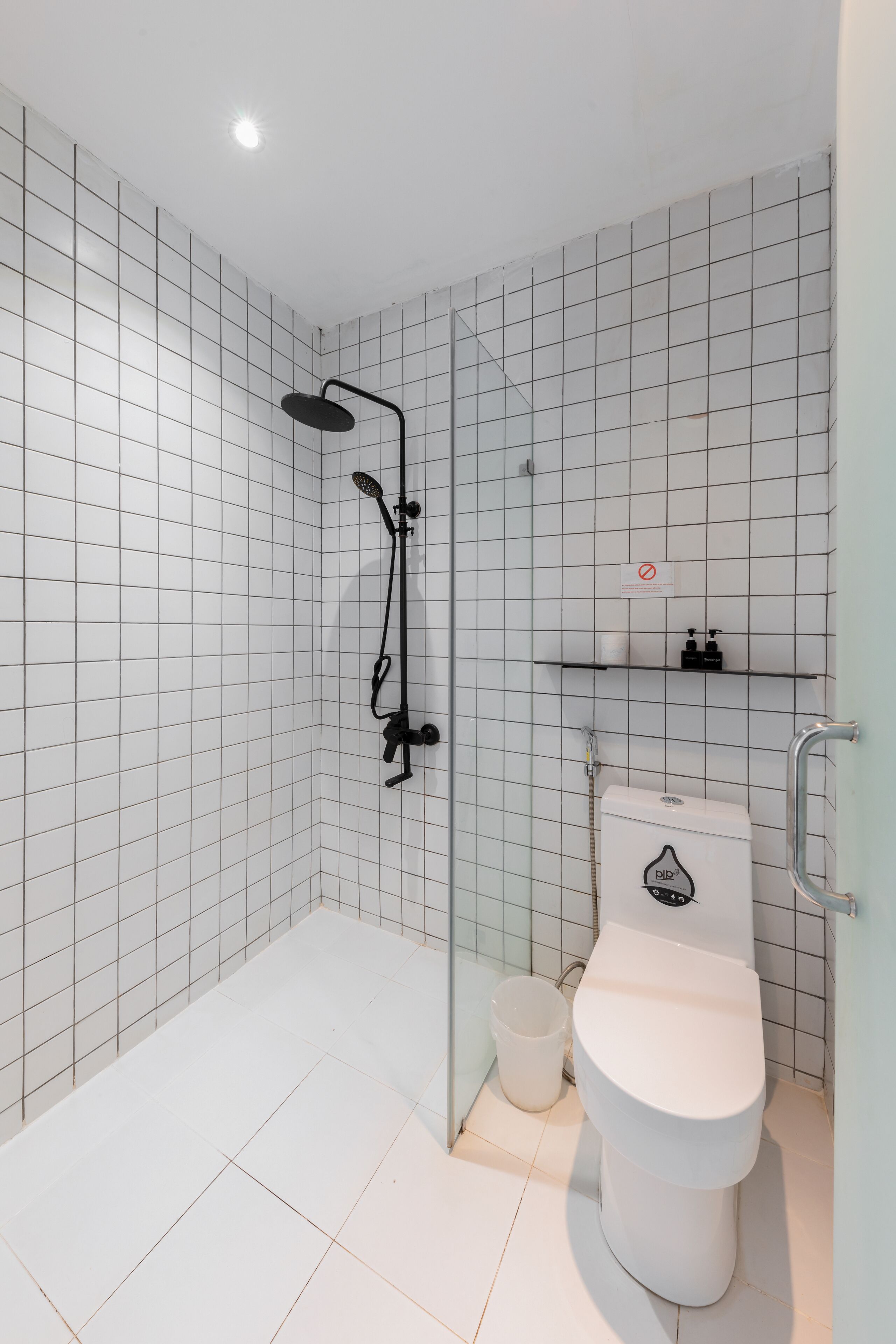 Une salle de bain moderne équipée d’une douche, de toilettes et d’une petite étagère où sont rangés les articles de toilette.