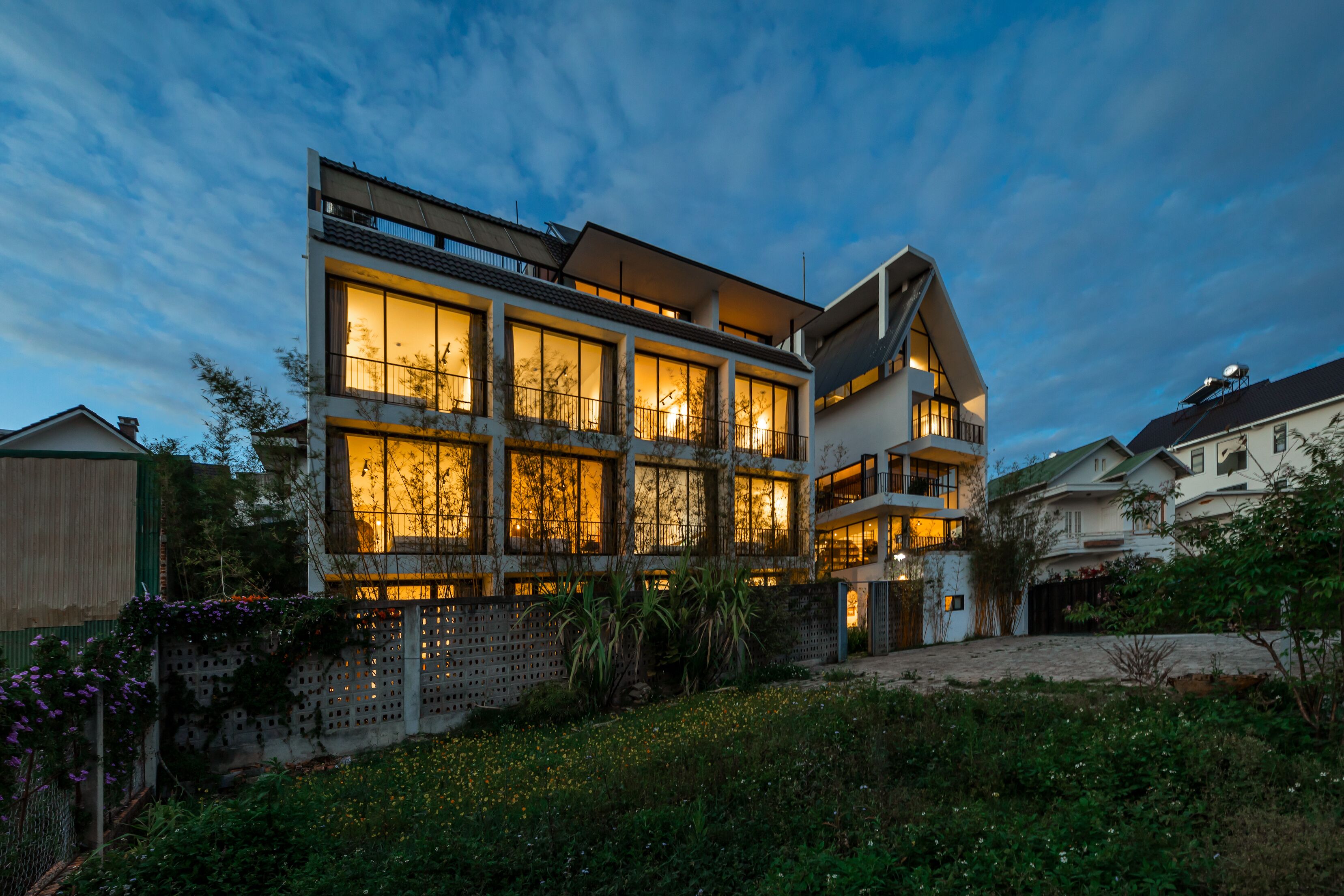 A modern multi-story building with large windows and balconies, surrounded by greenery.