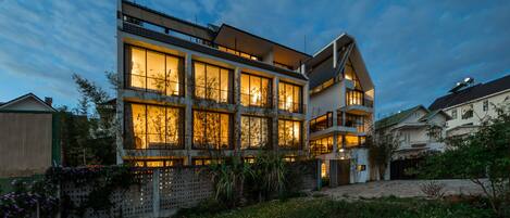 A modern multi-story building with large windows and balconies, surrounded by greenery.