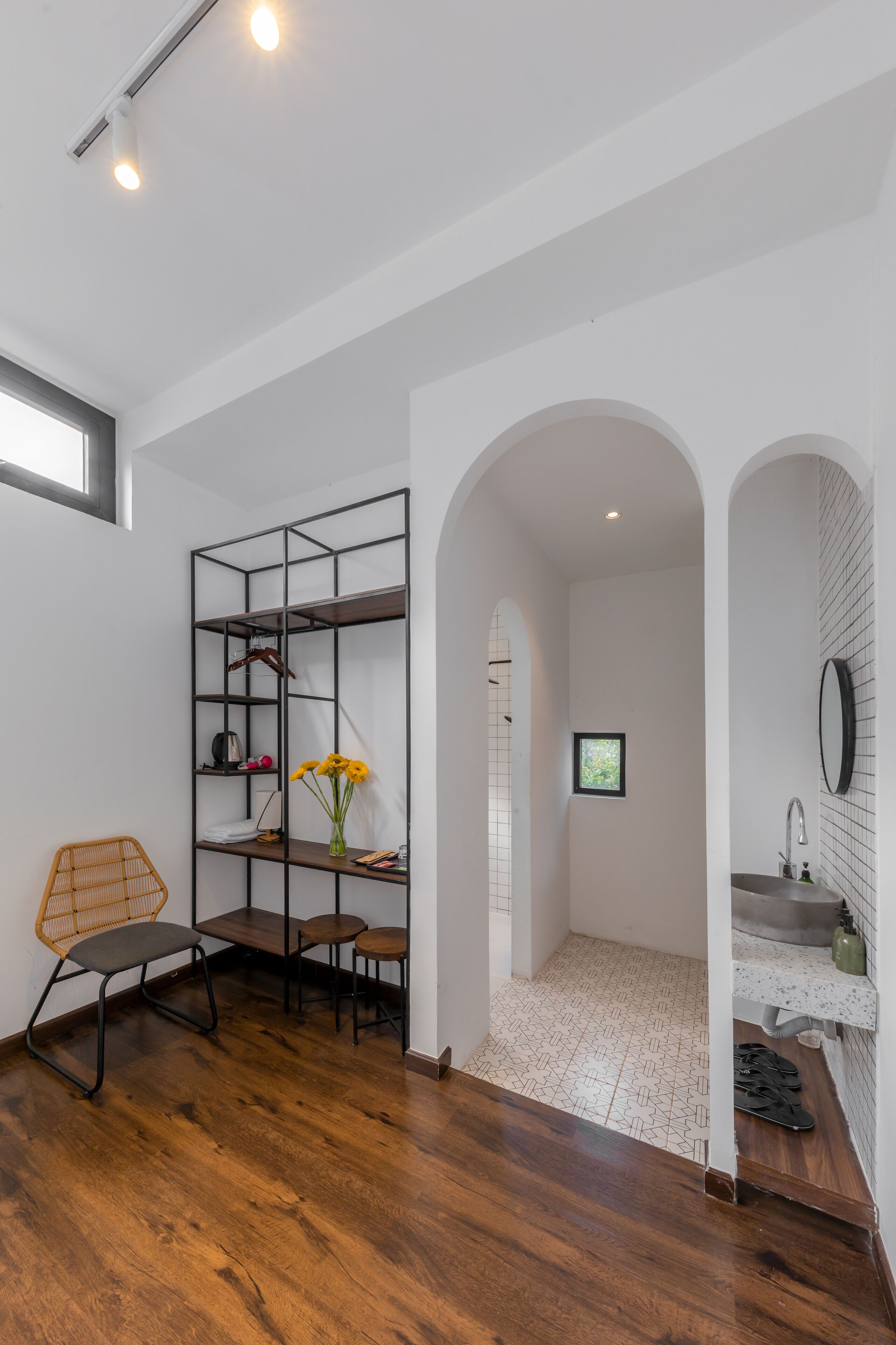 Un interior moderno con suelo de madera, una estantería metálica, una silla y una mesita con un florero.