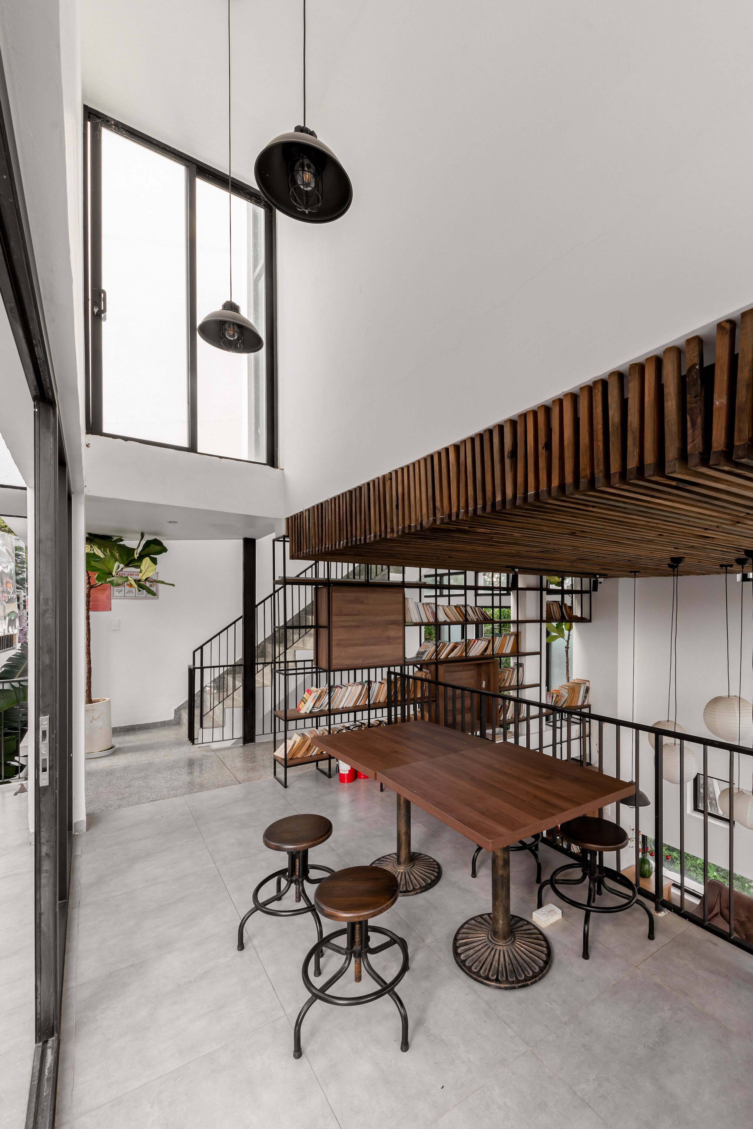 Un espace repas moderne avec une table en bois et des tabourets de bar, un escalier avec une rampe en bois et des luminaires suspendus.