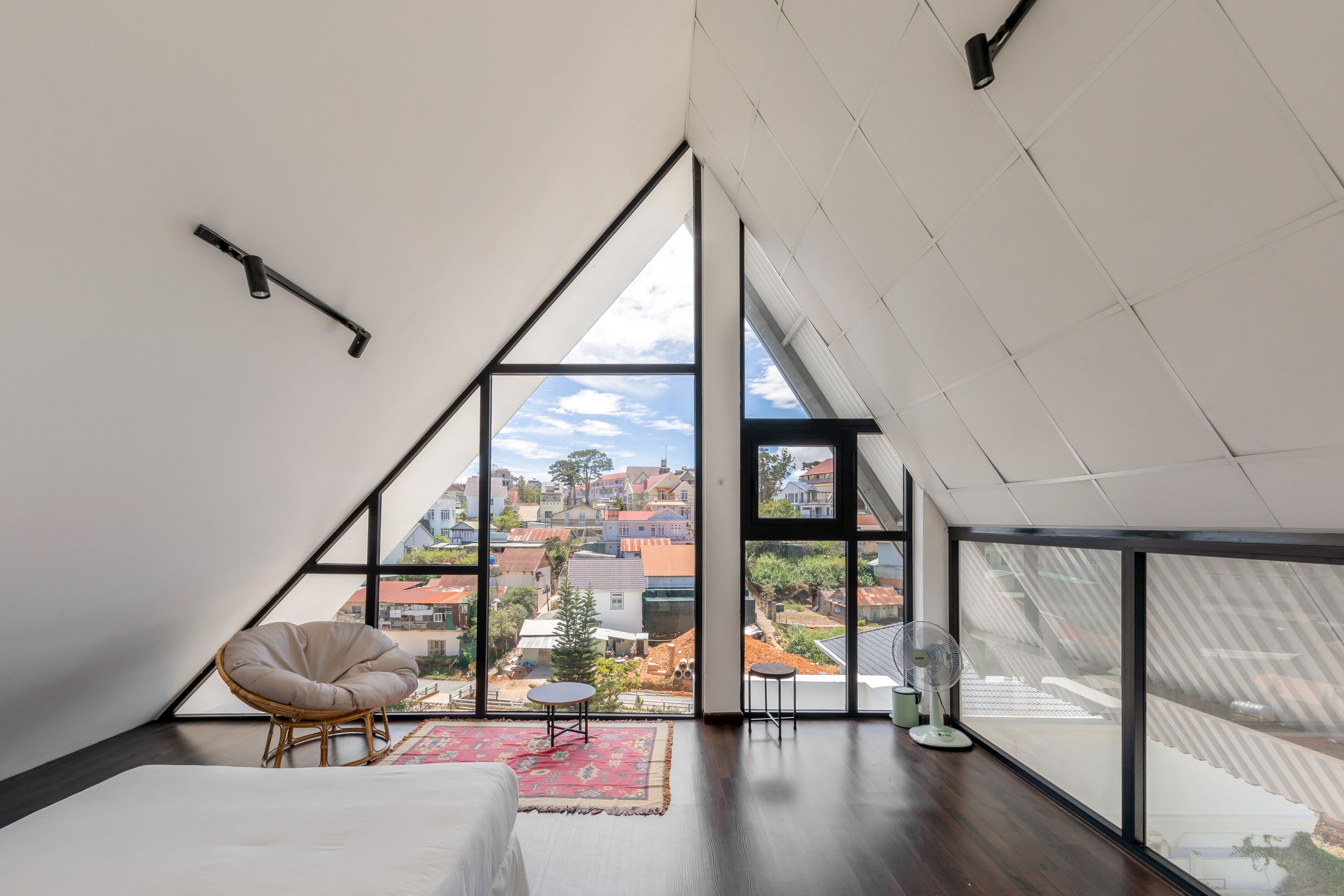 A modern loft bedroom with a large skylight, a bed, a chair, and a small table.