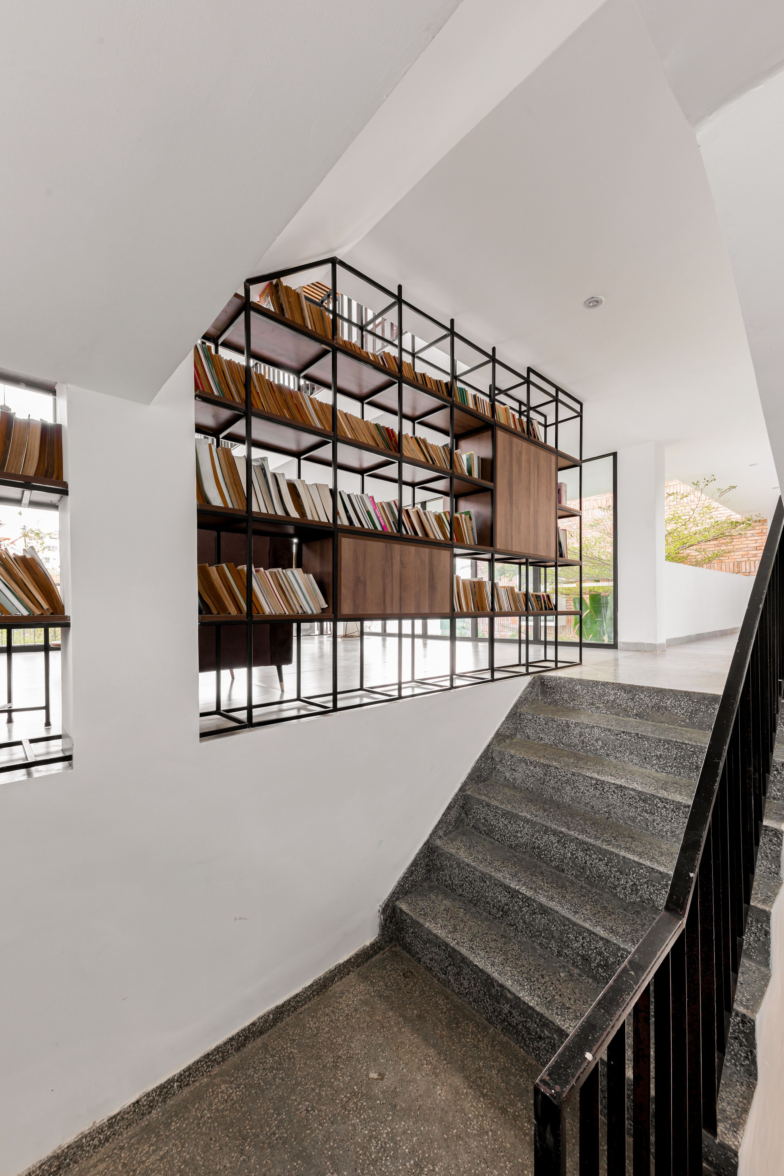 A modern interior with a staircase, a built-in bookshelf, and a view of the outdoors.