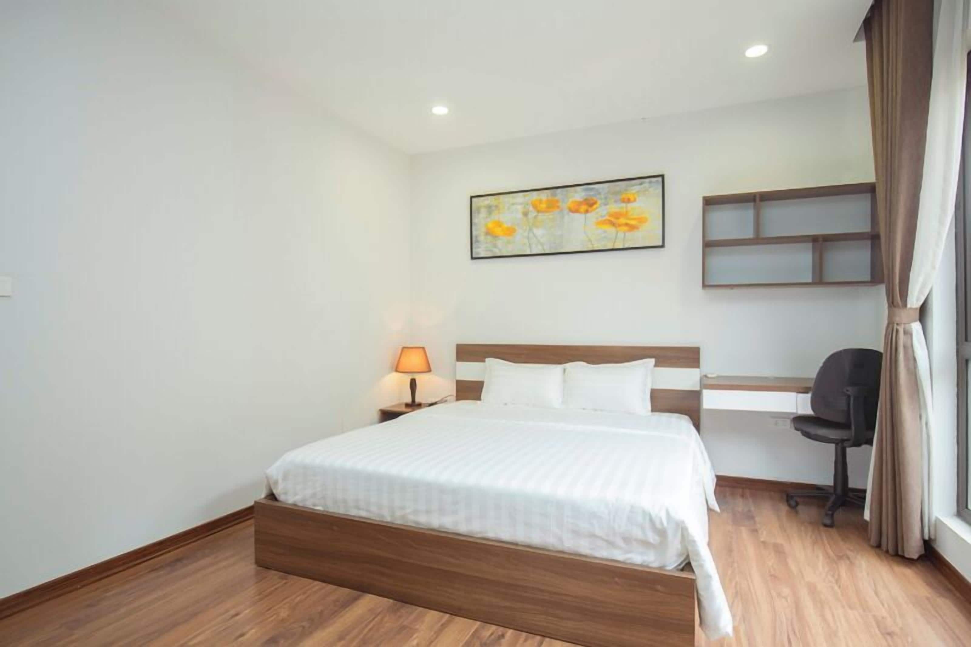 Habitación de hotel con cama de madera, escritorio, silla, lámpara y un cuadro en la pared.