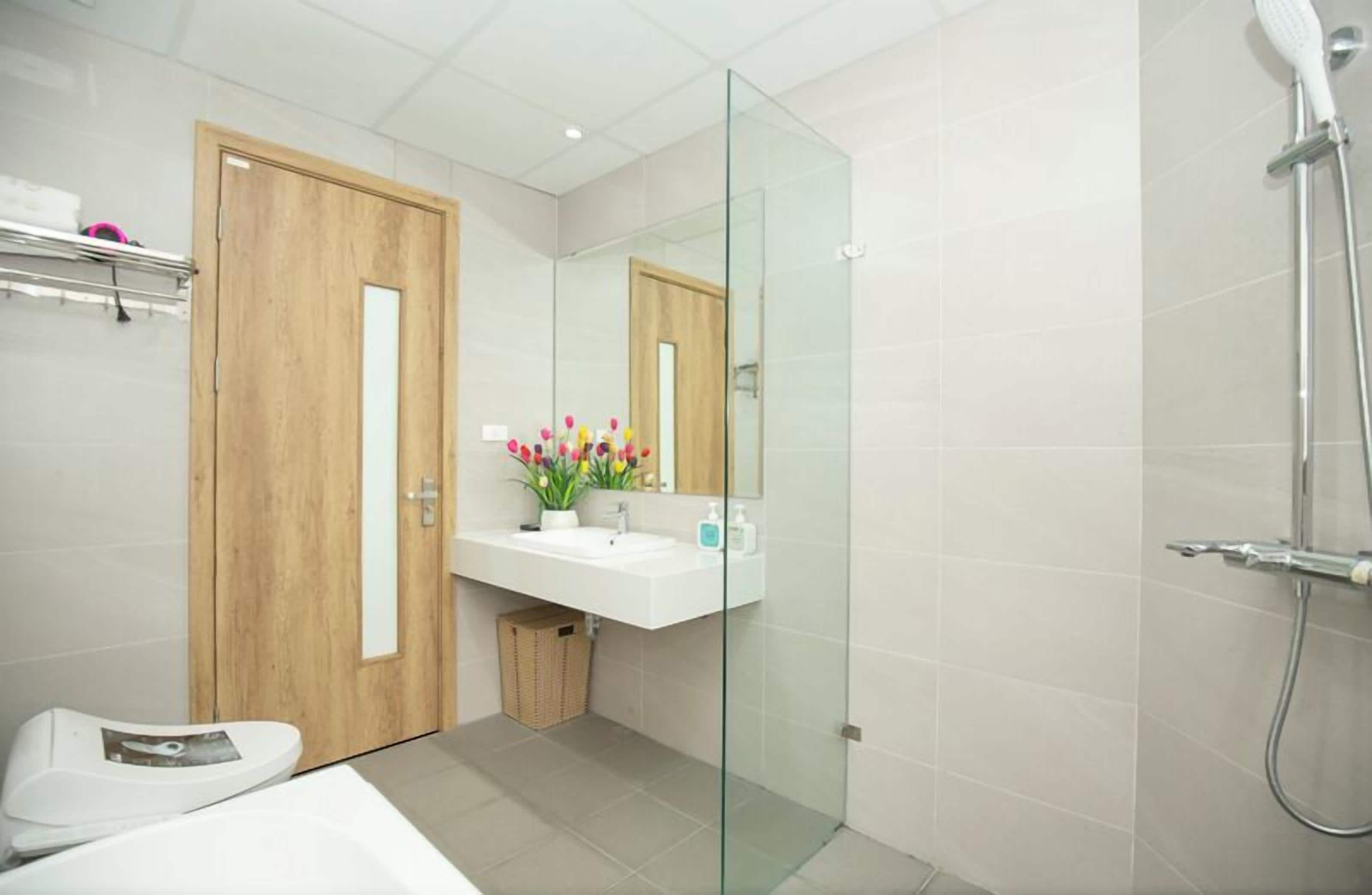 A modern bathroom with a wooden door, a glass shower enclosure, a white sink, and a toilet.