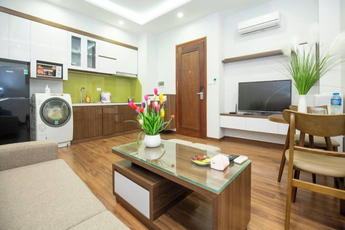 A modern living room with a glass coffee table, a TV, and a dining area with wooden chairs.