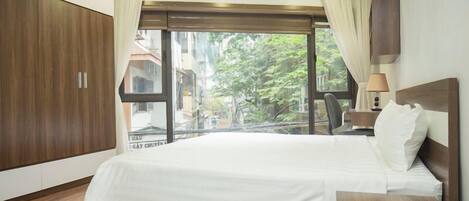 Habitación de hotel con una cama grande, un armario de madera y vistas a la ciudad a través de un ventanal.