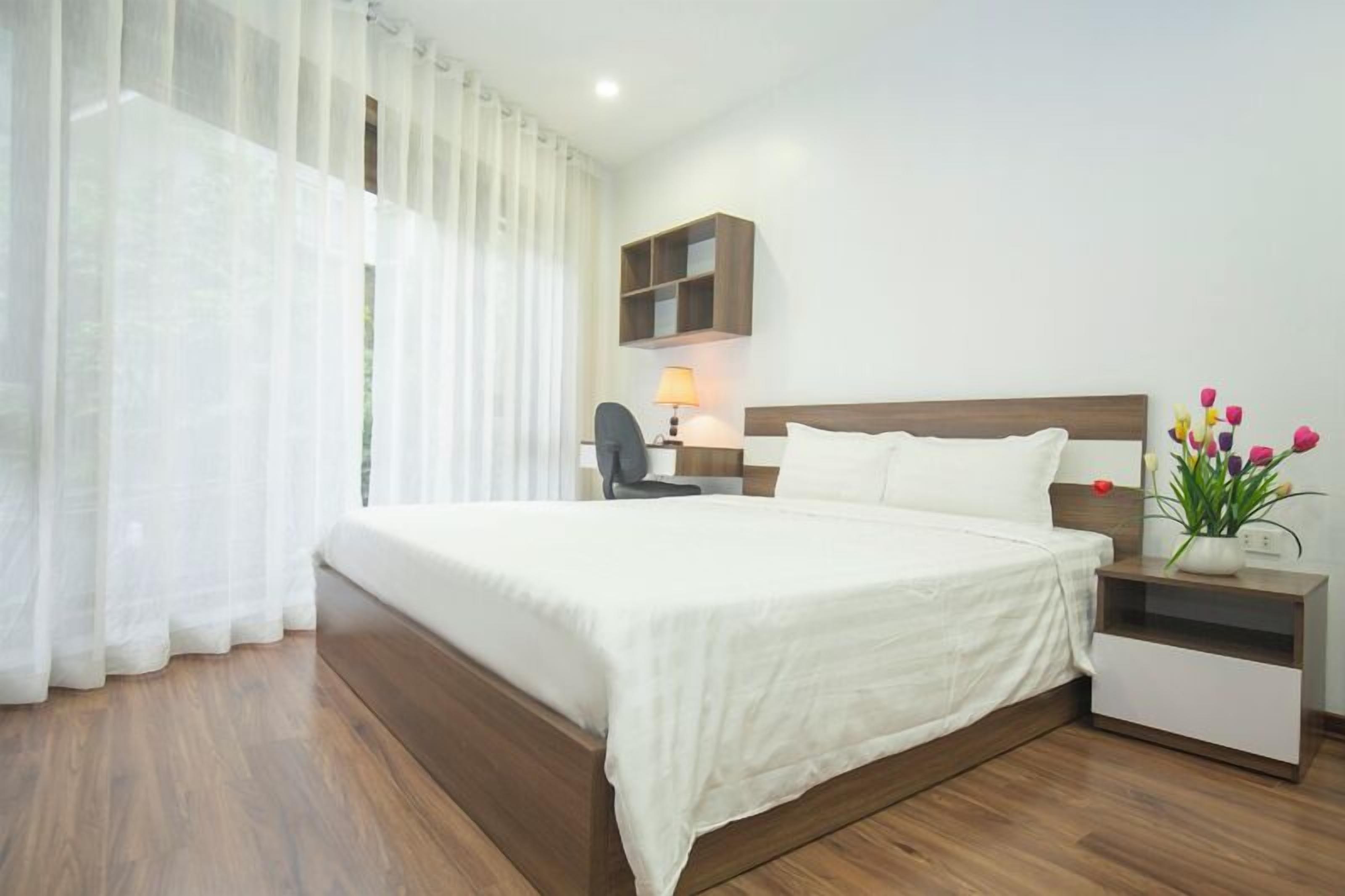 A neatly arranged hotel room with a large bed, a bedside table with a lamp, and a small shelf.