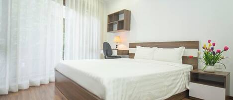 A neatly arranged hotel room with a large bed, a bedside table with a lamp, and a small shelf.