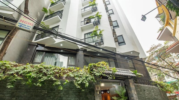 A modern building with a sign for NGH Hoang Huy, featuring balconies with plants, a stone facade, and a glass entrance.