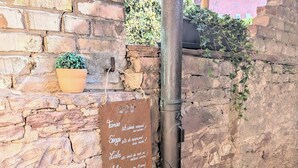 Un mur de pierres avec un tuyau en métal et une pancarte portant un texte en allemand.