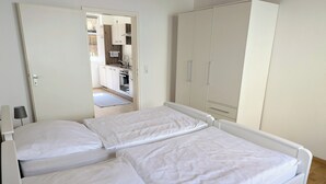 Un lit double avec une literie blanche, une armoire et une vue sur un coin cuisine.
