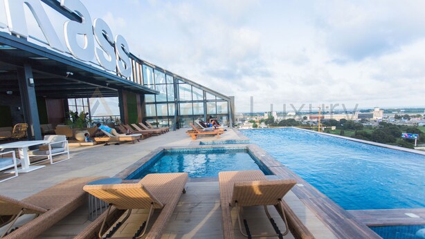 A rooftop pool area with lounge chairs and a glass building in the background. - Accra Luxury Apartments at Kass (Accra)