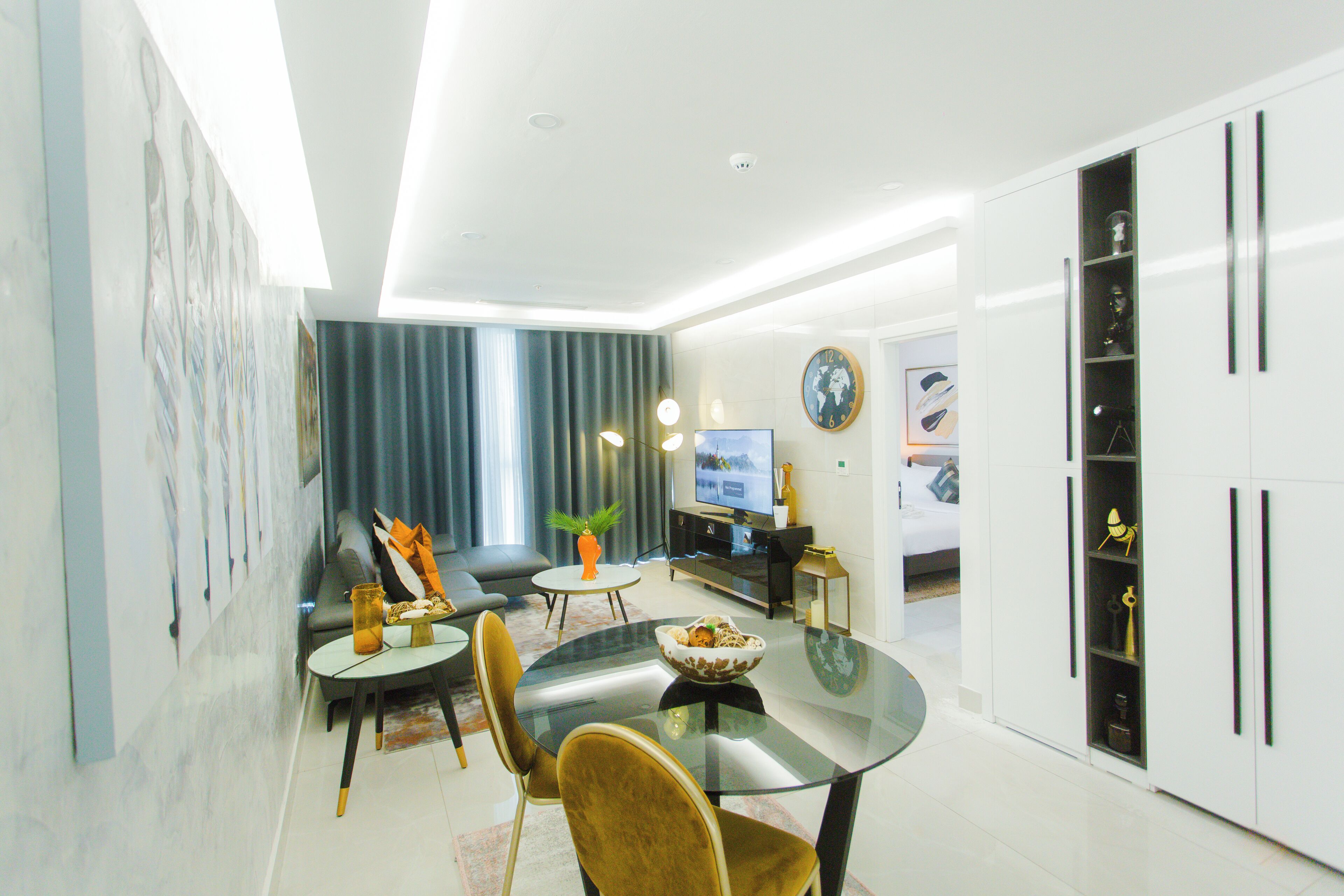A modern living room with a glass dining table, comfortable seating, a television, and a decorative plant.