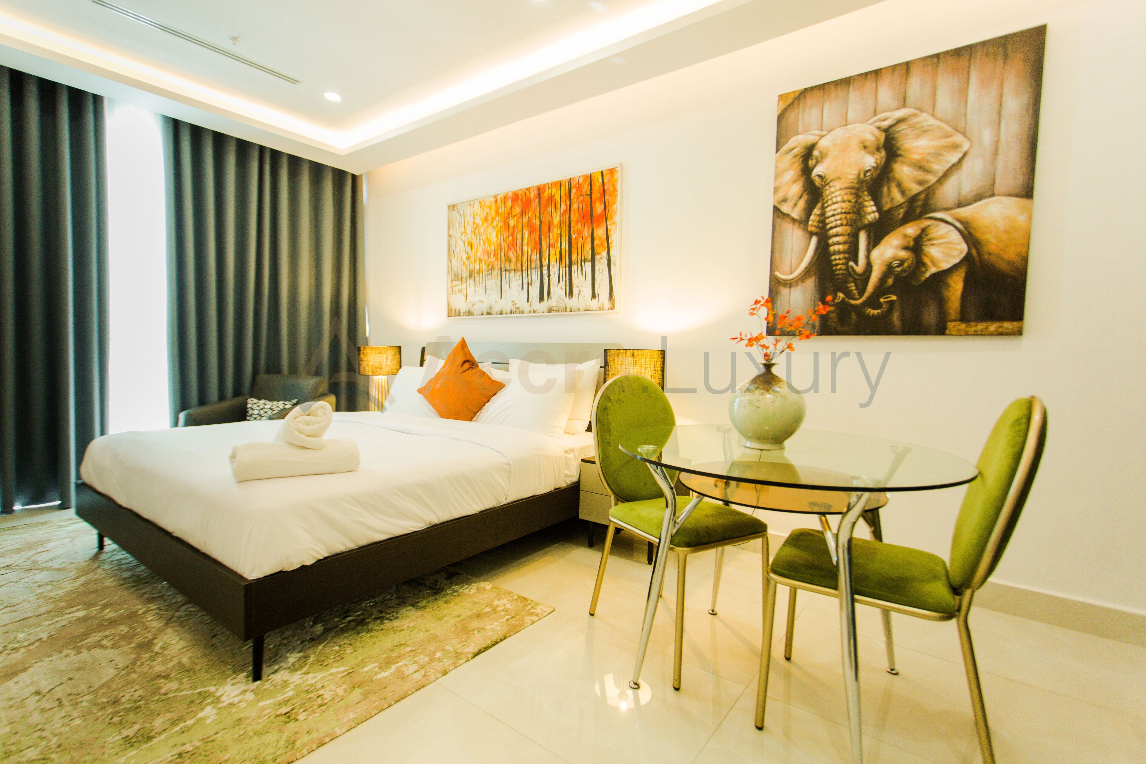 A modern hotel room with a large bed, a glass table, and two chairs.