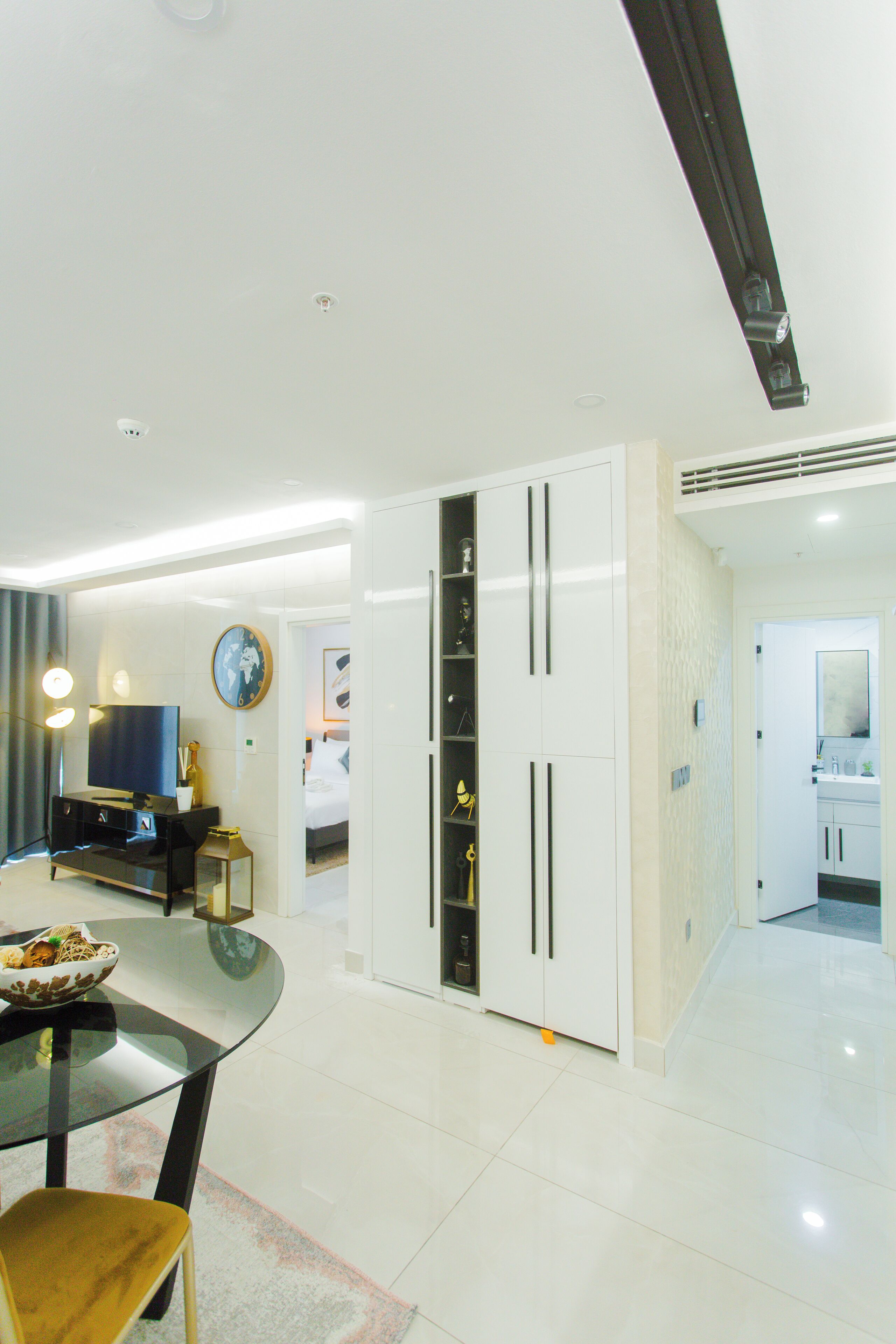 Quarto de hotel moderno com área de jantar, televisão, cama e banheiro visível por uma porta aberta.