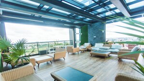 A spacious outdoor lounge area with wicker furniture, a glass ceiling, and a view of the city. - Accra Luxury Apartments at Kass (Accra)