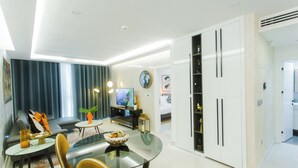 A modern living room with a glass dining table, a sofa, and a television. - Accra Luxury Apartments at Kass (Accra)