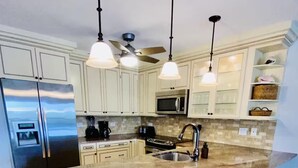 A modern kitchen with a large island, bar stools, a refrigerator, microwave, and a ceiling fan.