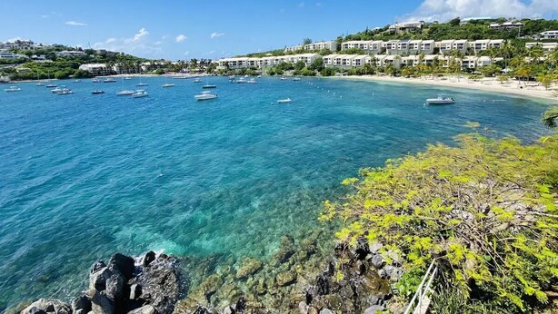 A coastal view with clear turquoise waters, boats, and a beachfront with buildings.