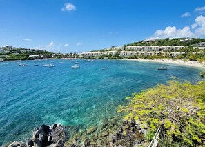 A coastal view with clear turquoise waters, boats, and a beachfront with buildings.