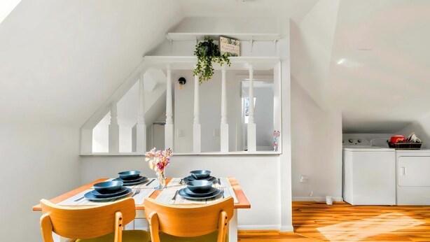 A dining area with a wooden table set for two, a window with white railings, and a kitchen area with appliances. - Charming 1 BR Atlanta Retreat: Minutes to Midtown (Atlanta)