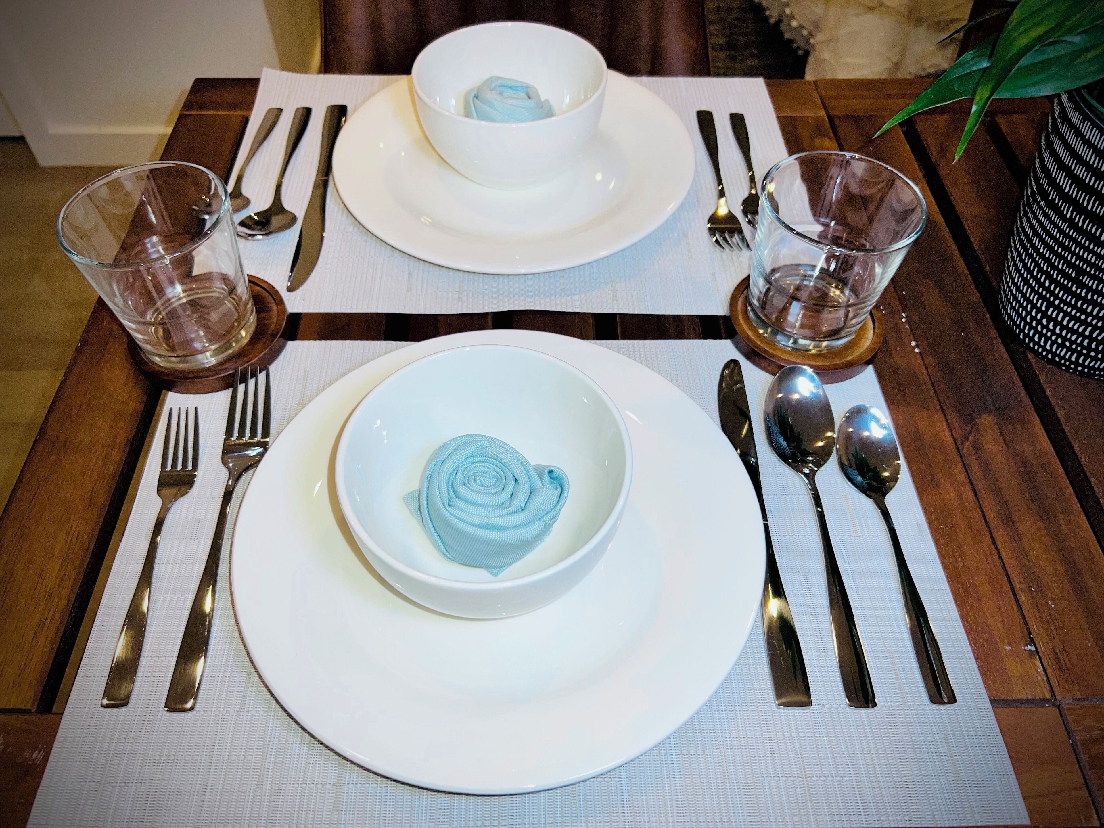 Une table à manger dressée avec de l’assiette blanche, des bols, des couverts et des verres.
