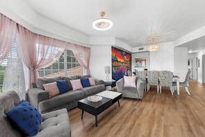 Una sala de estar moderna con un sofá gris, una mesita de centro y una zona de comedor con mantel estampado.