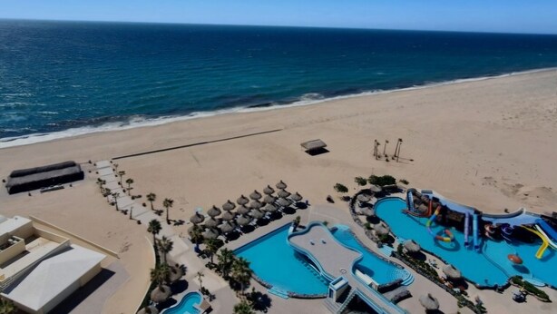 A beach resort with multiple swimming pools, sun loungers, and a clear view of the ocean.
