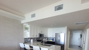 A modern kitchen with white cabinets, a central island with bar stools, a microwave, and a refrigerator.