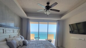 A bedroom with a bed, a ceiling fan, a TV, and a view of the ocean.