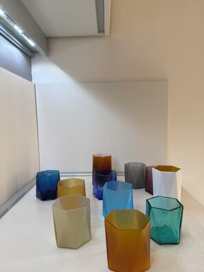A room with a white table displaying various geometric glass vases. - The Gardener's Pavilion (Venezia)