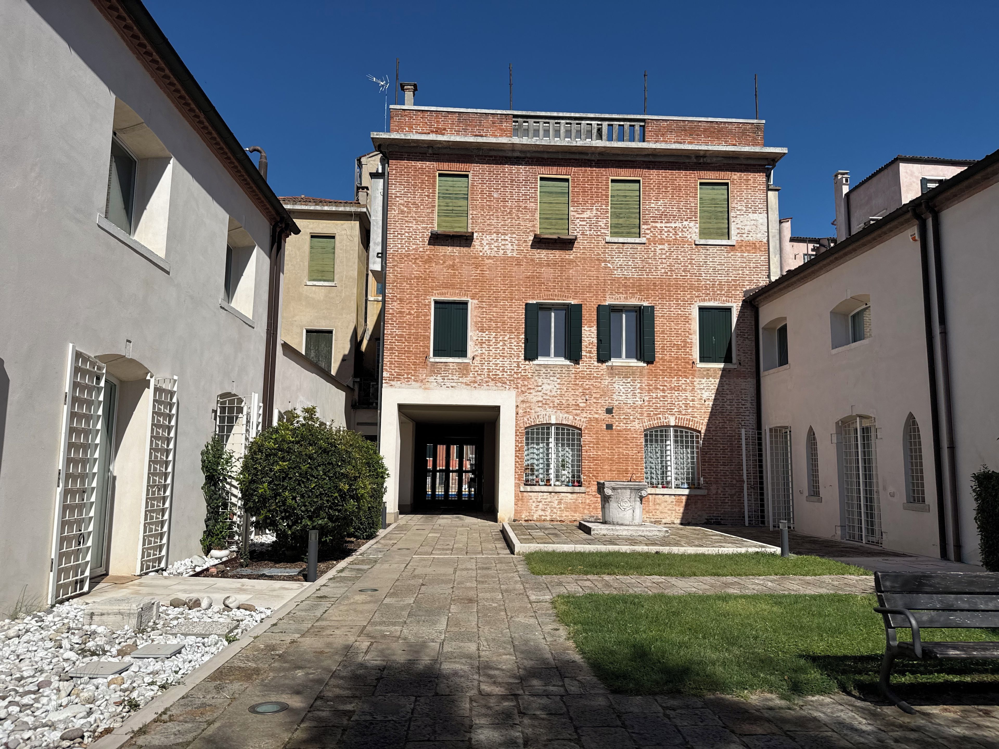 Une cour intérieure avec un bâtiment central doté d’une façade en briques, de nombreuses fenêtres avec volets et d’une petite statue à l’avant.