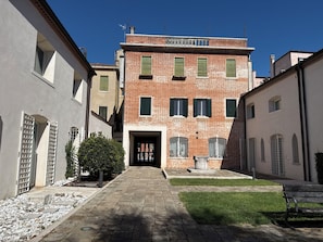 A courtyard with a central building featuring a brick facade, multiple windows with shutters, and a small statue in front. - The Gardener's Pavilion (Venezia)