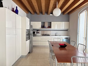 A modern kitchen with white cabinetry, a wooden dining table, and a hanging light fixture.