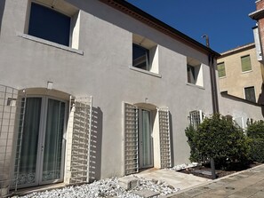 A building with multiple windows, some with shutters, and a small garden area with pebbles.