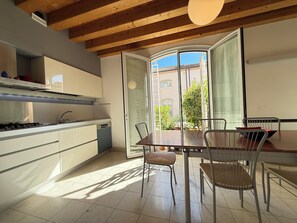 A modern kitchen with a dining area, featuring a large window, wooden ceiling beams, and a tiled floor. - The Gardener's Pavilion (Venezia)