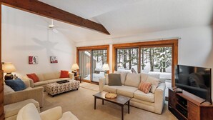 Una sala de estar acogedora con un sofá, sillones, una mesita de centro y un televisor. Amplias ventanas ofrecen vistas a un paisaje nevado.