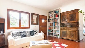 Een woonkamer met een witte bank, een rood-wit geruit tapijt, een houten kast en een boekenplank vol boeken.